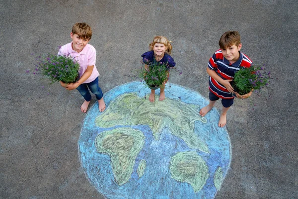 Niña preescolar y dos niños de la escuela con flores en la tierra globo pintura con tiza de colores en el suelo. Feliz concepto del día de la tierra. Creación de niños para salvar el mundo, ecología del medio ambiente. —  Fotos de Stock