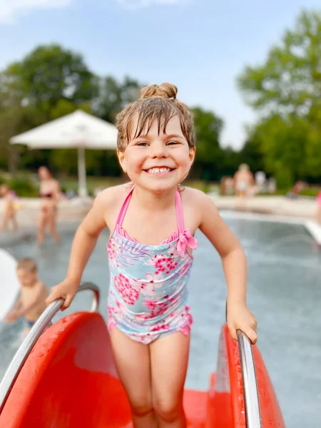 Маленькая дошкольница плескается в открытом бассейне в теплый летний день. Счастливый здоровый малыш наслаждается солнечной погодой в городском общественном бассейне. Активность детей на открытом воздухе с водой. — стоковое фото