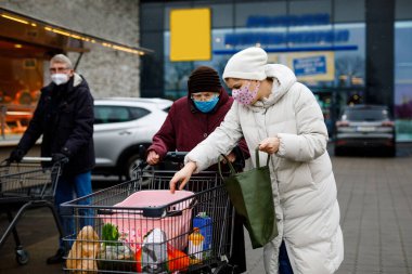 Kıdemli kadın ve tıbbi maskeli sosyal hizmetler görevlisi pandemik koronavirüs hastalığı nedeniyle. Kızı ya da torunu süpermarkette alışveriş yaparken büyükannesine yardım ediyor, market arabasında yiyecek satıyor, açık havada geziyor.