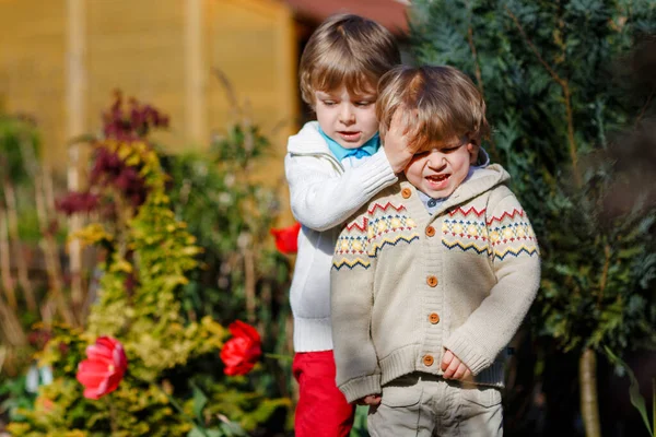 Twee broertjes vechten en hebben ruzie. Kleuterschool, overstuur kinderen die buiten ruziën. Rivaliteit en concurrentie tussen broers en zussen. Ongelukkige tweeling. Een huilende jongen — Stockfoto