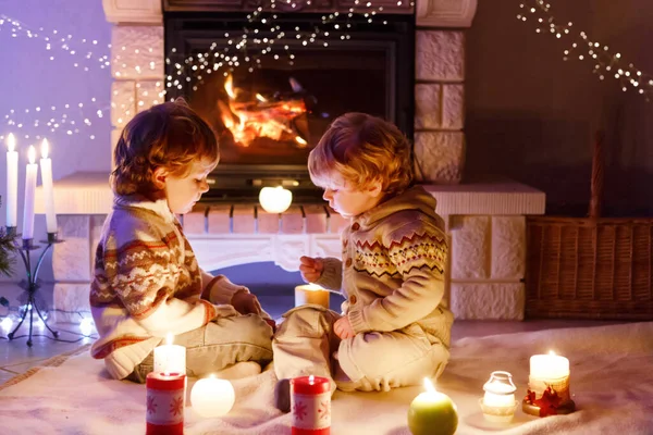 Ragazzi carini, gemelli biondi che giocano insieme e guardano in fiamme nel camino. Famiglia che celebra la festa di Natale — Foto Stock