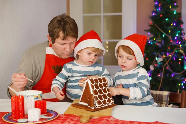 Pai e dois filhos pequenos decorando uma casa de biscoitos de gengibre — Fotografia de Stock