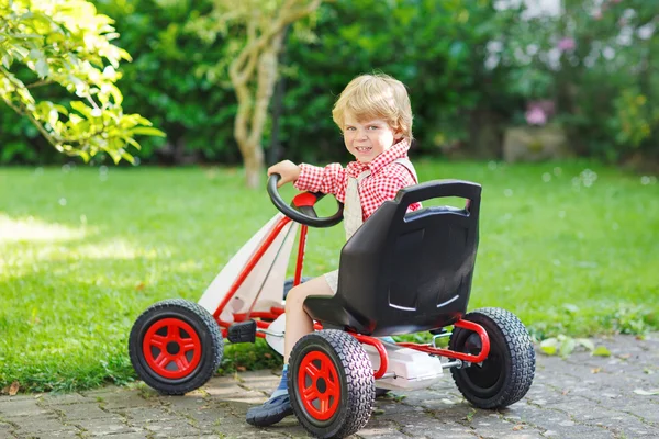 Active little boy driving pedal car in summer garden — Stock Photo, Image