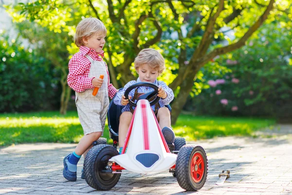 Two little sibling boys playing with pedal car in home's garden — Stock Photo, Image