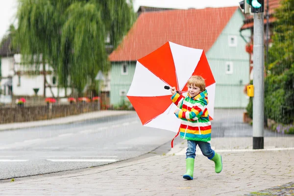 Criança bonita com guarda-chuva vermelho e casaco colorido ao ar livre um — Fotografia de Stock