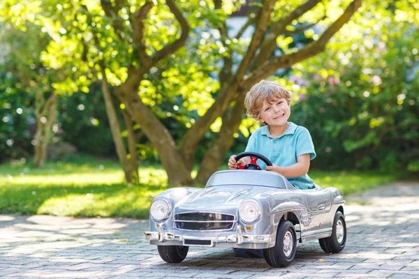 Kleiner Junge fährt großes Spielzeugauto im Freien lizenzfreie Stockbilder