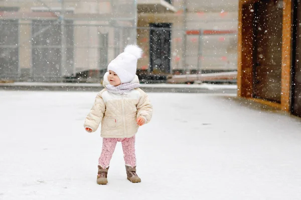 Bonne petite fille qui fait ses premiers pas à l'extérieur en hiver à travers la neige. Bébé mignon apprenant à marcher. Enfant qui s'amuse par temps froid et neigeux. Bébés première neige, activité. Promenade hivernale en plein air — Photo