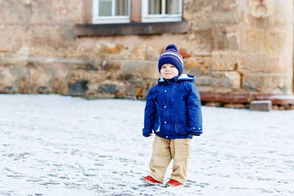 Piccolo bambino che cammina per la città innevata durante le nevicate. Carino bambino felice in abiti invernali divertirsi all'aperto, nella giornata fredda con la neve per strada. — Foto Stock