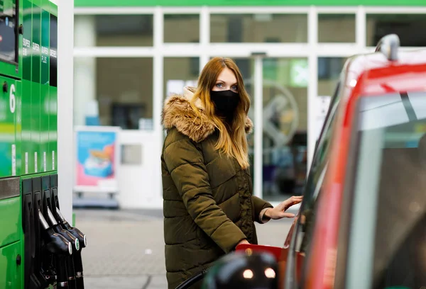 Las mujeres usan máscara médica en la gasolinera de autoservicio, sostienen la boquilla de combustible, repostan el auto con gasolina durante el bloqueo pandémico del virus corona. Las personas con máscaras como medida preventiva y protección covid — Foto de Stock