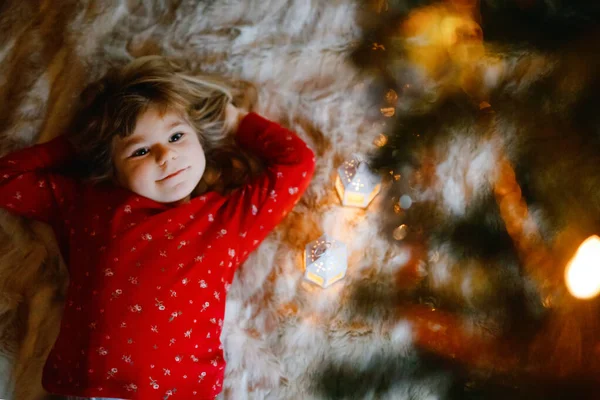 小可爱的小女孩穿着睡衣在圣诞树下梦见圣诞老人在家里，在室内。传统的基督教家庭节。快乐的学龄前儿童在圣诞节等待礼物。舒适柔和的光线 — 图库照片