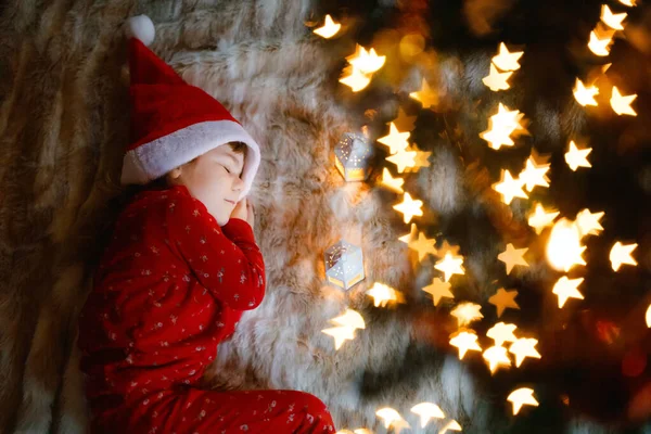 Pequena menina criança bonito em pijama sob a árvore de Natal e sonhando com o Papai Noel em casa, dentro de casa. Festival tradicional da família cristã. Criança pré-escolar feliz esperando presentes em xmas. Luz suave aconchegante — Fotografia de Stock