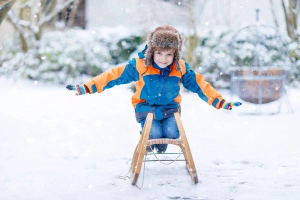 Niño disfrutando del paseo en trineo durante las nevadas. Feliz niño en edad preescolar montado en trineo vintage. Niño jugar al aire libre con nieve. Diversión activa para vacaciones de Navidad en familia en invierno — Foto de Stock