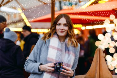 Güzel genç bir kadın sıcak punç içiyor, Alman Noel pazarında sıcak şarap içiyor. Kış kıyafetleri içinde mutlu bir kız. Arka planda ışıklar var. Berlin, Almanya 'da kış günü kar tatilinde..