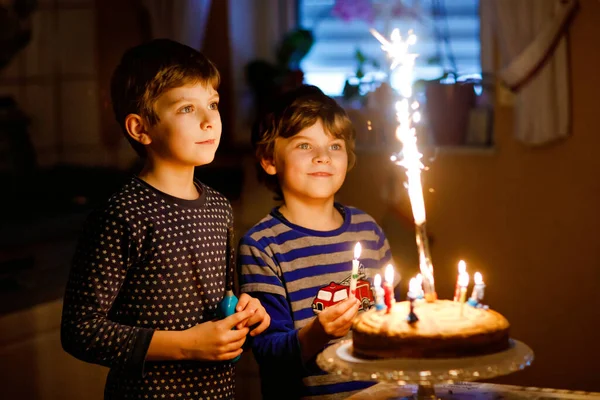 两个漂亮的孩子，学龄前的小男孩庆祝生日，并在自家做的烤蛋糕上吹点蜡烛，室内。兄弟姐妹孩子的生日聚会。快乐的孪生兄弟，在焦糖上放烟火. — 图库照片
