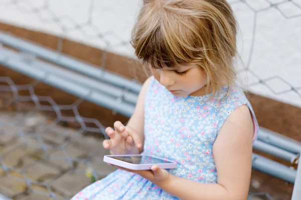 Nettes kleines Mädchen spielt mit Smartphone Gesundes Baby berührt Handy mit den Fingern, sucht Cartoons und hat Spaß mit pädagogischen Apps. Kind im Garten im Freien — Stockfoto