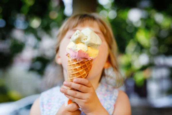 Little preschool girl eating ice cream in waffle cone on sunny summer day. Happy toddler child eat icecream dessert. Sweet food on hot warm summertime days. Bright light, colorful ice-cream — Stock Photo, Image