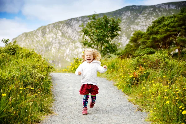 Cute little happy toddler girl running on nature path in Glenveagh national park in Ireland. Smiling and laughing baby child having fun spending family vacations in nature. Traveling with small kids — Stock Photo, Image