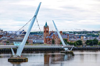 Derry, İrlanda. Kuzey İrlanda 'da, Derry Londonderry' de, Kültür Şehri 'nde şehir merkezinde aydınlatılmış bir barış köprüsü. Gece bulutlu gökyüzü, alacakaranlıkta nehirde yansıyor.