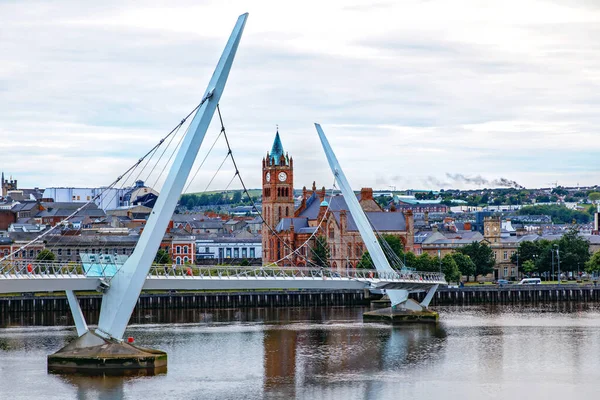 Derry, Irlanda. Ponte della pace illuminato a Derry Londonderry, città della cultura, in Irlanda del Nord con il centro della città sullo sfondo. Cielo nuvoloso notturno con riflesso nel fiume al crepuscolo — Foto Stock