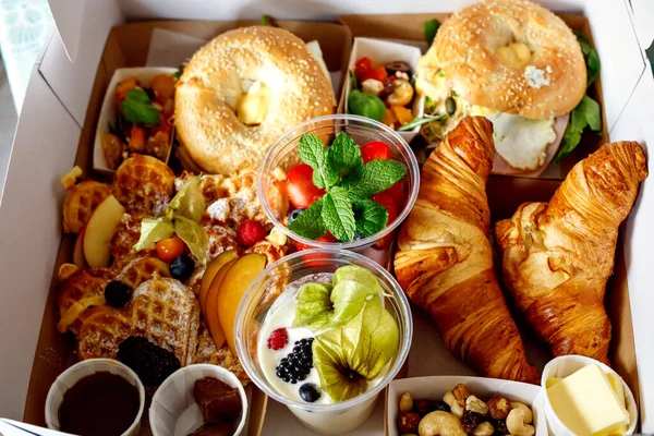 Ontbijt in een doos om te gaan van gesloten restaurant als gevolg van corona virus lockdown. Verse bagels, croissants, bessen, salade en groenten voor een romantische lunch. Eten om te gaan picknicken. — Stockfoto