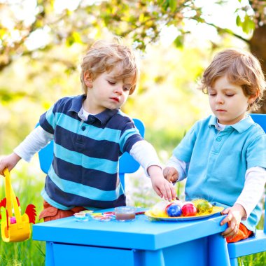İki küçük çocuk Paskalya tavşanı kulakları takıyor, renkli yumurta boyuyorlar.