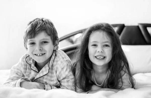Két boldog gyerek pizsamában ünnepli a pizsamapartit. Óvodás és iskolás fiú és lány jól érzik magukat együtt.. — Stock Fotó