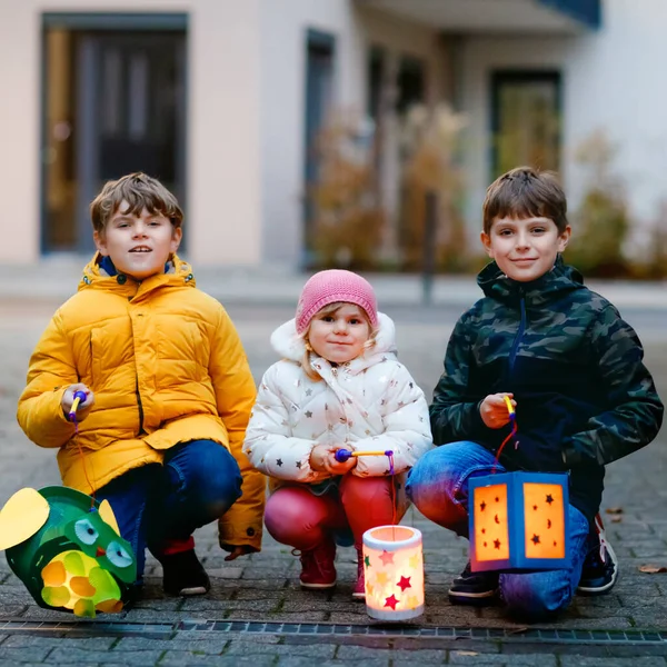 Kleine Mädchen und zwei Jungen halten selbstgebastelte Laternen mit Kerzen für den Martinsumzug in der Hand. Drei gesunde Kinder freuen sich über Familienumzug im Kindergarten Traditioneller Martinsumzug — Stockfoto