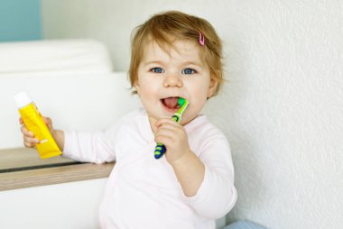 Küçük kız diş fırçası tutuyor ve ilk dişlerini fırçalıyor. Bebek süt dişini temizlemeyi öğreniyor. Önleme, hijyen ve sağlık hizmetleri kavramı. Banyoda mutlu bir çocuk