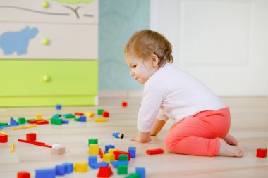 Eğitici oyuncaklarla oynayan tatlı bir kız bebek. Mutlu sağlıklı çocuk evde ya da çocuk odasında renkli tahta bloklarla eğleniyor. Bebek sürünüyor, arkadan bakıyor, yüzü yok, tanınmaz halde.