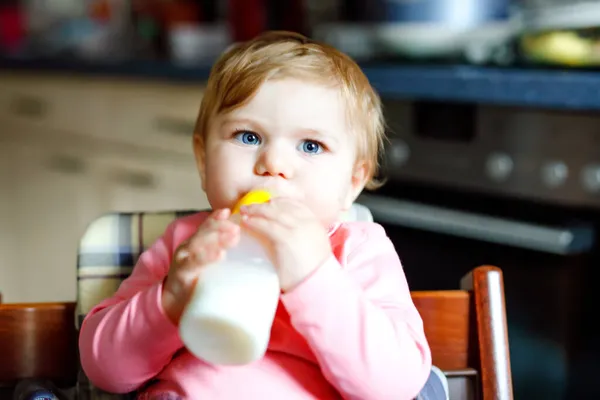 Schattig schattig baby meisje met borstvoeding fles en drinken formule melk. Eerste voedsel voor baby 's. Pasgeboren kind, zittend in stoel van de huishoudelijke keuken. Gezonde baby 's en flesvoeding — Stockfoto