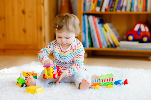 Pequena menina brincando com brinquedos educativos de madeira em casa ou berçário. Criança com trem colorido. Criança se divertindo com brinquedos diferentes. Criança solitária durante quarentena pandêmica do vírus da corona — Fotografia de Stock