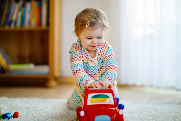 Malá holčička si hraje se vzdělávacími dřevěnými hračkami doma nebo v jeslích. Batole s barevným červeným autem. Dítě se baví s různými hračkami. Osamělé dítě během pandemické karantény viru korony — Stock fotografie