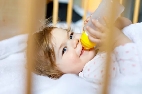 Linda niña sosteniendo biberón con fórmula suave y beber. Niño en cuna antes de dormir — Foto de Stock