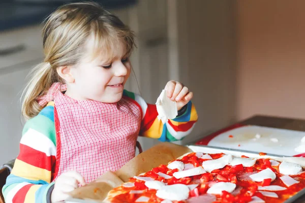 Adorable little toddler girl making italian pizza at home. Cute happy child having fun in home kitchen, indoors. Kid, preschooler helping and preparing healthy meal — Stock Photo, Image