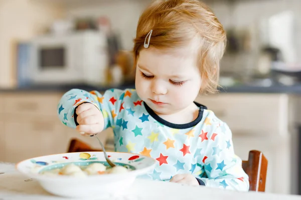 Adorable niña comiendo sopa de fideos vegetales con cuchara. alimento, niño, alimentación y desarrollo. Lindo niño, hija con cuchara sentada en silla alta y aprender a comer por sí mismo. — Foto de Stock