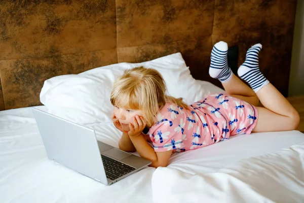 학교다니는 여자 애가 컴퓨터, 공책, 침대에 있는 깨끗 한 흰색 리넨을 보고 있습니다. 자녀들 과의 실내 활동. 프리랜서, 학습 거리, 또는 집에서 아이들의 개념을 가지고 일하는 것. 행복 한 아이 — 스톡 사진