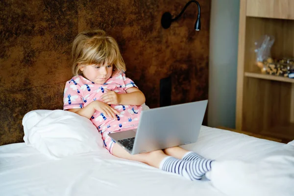Preschool girl watching videos on laptop, notebook,in bed on clean white linens. Indoors activity with children. Freelance, distance learning or work from home with kids concept. Happy child — Stock Photo, Image