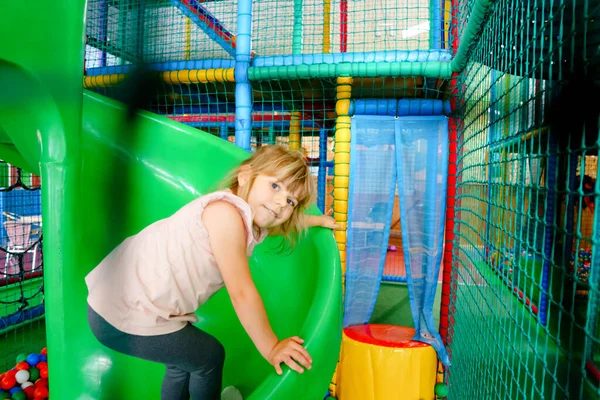 Rapariga activa a brincar no recreio interior. Criança pré-escolar alegre feliz escalando, correndo, pulando e se divertindo com bolas plásticas coloridas. Atividades internas para crianças. — Fotografia de Stock