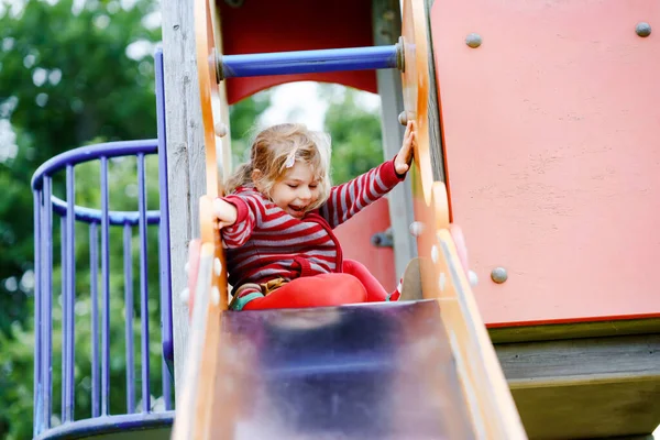 Little preschool girl playing on outdoor playground. Happy toddler child climbing and having fun with summer outdoors activity. Girl slinding down the slide. — Stock Photo, Image
