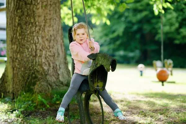 Happy little preschool girl having fun on swing in domestic garden. Healthy toddler child swinging on summer day. Children activity outdoor, active smiling kid laughing. Old tires as swing. — Stock Photo, Image