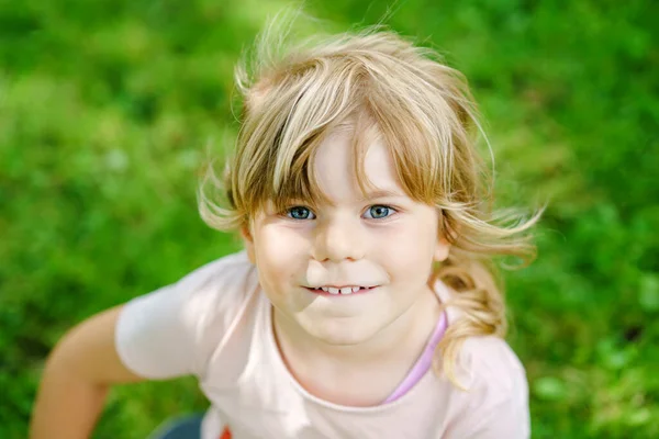 Egy boldog mosolygós óvodás lány portréja a szabadban. Egy szőke hajú kisgyerek, aki a kamerába néz és mosolyog. Boldog egészséges gyermek élvezze a szabadtéri tevékenység és a játék. — Stock Fotó