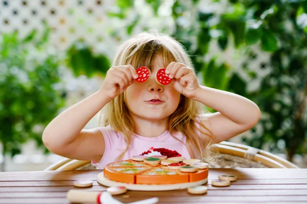 Маленькая милая девочка играет с деревянной игрушечной пиццей. Дошкольный ребенок веселится с детьми деятельности, как, играть с едой, в помещении. — стоковое фото