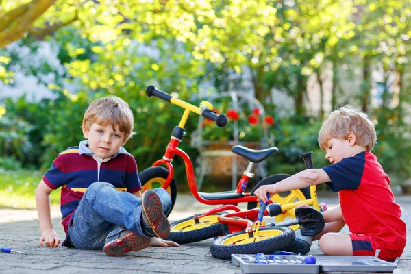 행복 한 두 꼬마 소년 이 자전거의 체인을 수리하고 균형 자전거의 바퀴를 교환하는 모습 — 스톡 사진