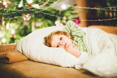 Noel ağacının altında uyuyan ve Noel Baba 'yı evde, evde hayal eden tatlı sarışın çocuk. Geleneksel Hıristiyan festivali. Mutlu çocuk Noel 'de hediye bekliyor. Samimi yumuşak ışık