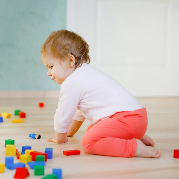 Linda niña jugando con juguetes educativos. Feliz niño sano que se divierte con diferentes bloques de madera de colores en casa o guardería. Bebé gateando, vista desde atrás, sin rostro, irreconocible —  Fotos de Stock