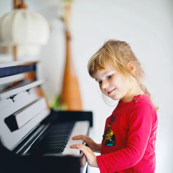 Vacker liten flicka som spelar piano i vardagsrummet. Söta förskolebarn som har roligt med att lära sig spela musikinstrument. Tidig musikundervisning för barn. — Stockfoto