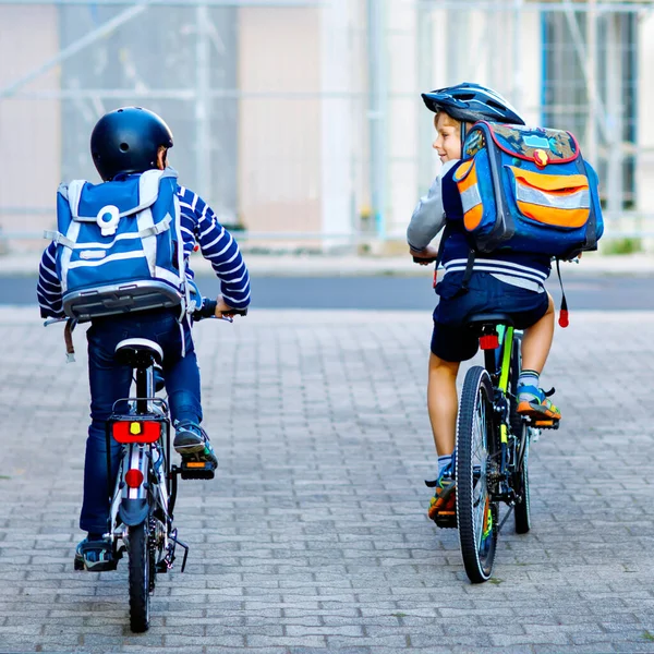 Deux écoliers en casque de sécurité à vélo dans la ville avec des sacs à dos. Enfants heureux en vêtements colorés faisant du vélo sur le chemin de l'école. Moyens sûrs pour les enfants à l'extérieur de l'école — Photo