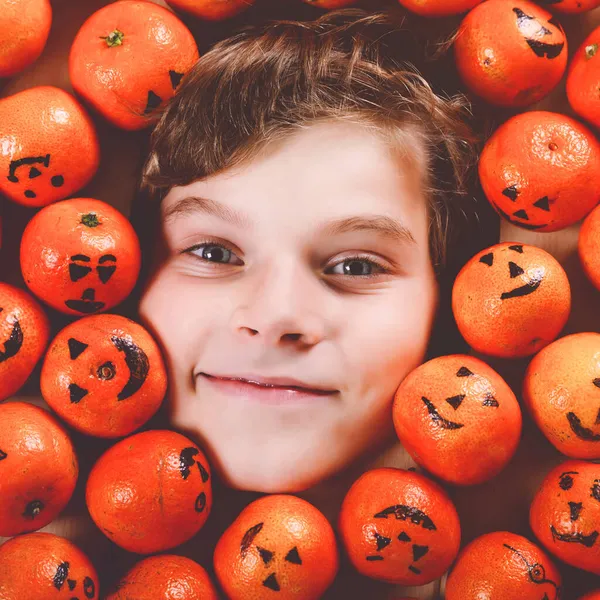 Забавный портрет очаровательного мальчика с апельсиновым мандарином, выглядящим как маленькая тыква-фонарь. Счастливая улыбка ребенка праздник Хэллоуин фестиваль или вечеринка. Создание открыток для друзей. — стоковое фото