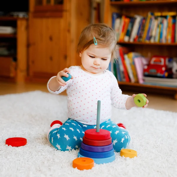 Адекватная симпатичная маленькая девочка, играющая с учебными деревянными игрушками дома или в детском саду. Туфелька с разноцветной стопкой пирамид и музыкальной игрушкой. Счастливый здоровый ребенок веселится с разными игрушками — стоковое фото