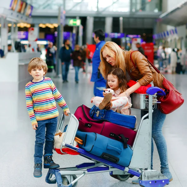 Zwei kleine Kinder, Junge und Mädchen, Geschwister und Mutter am Flughafen. Kinder, Familie auf Reisen, Urlaub mit dem Flugzeug und Warten auf Trolley mit Koffern, die von Frau am Terminal auf Flug geschoben werden. — Stockfoto
